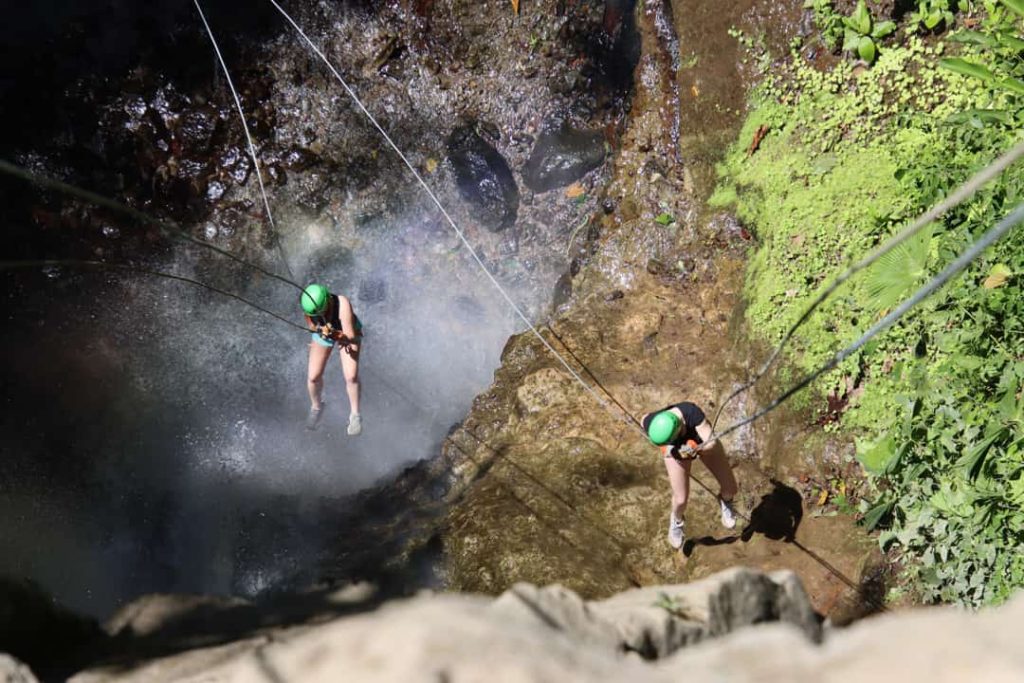 Twee mensen met een groene helm laten zich aan touwen zakken langs een waterval in een rotsachtige kloof