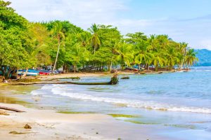 Wit zandstrand met palmbomen, kleine bootjes en helder turquoise water aan de Caribische kust van Costa Rica