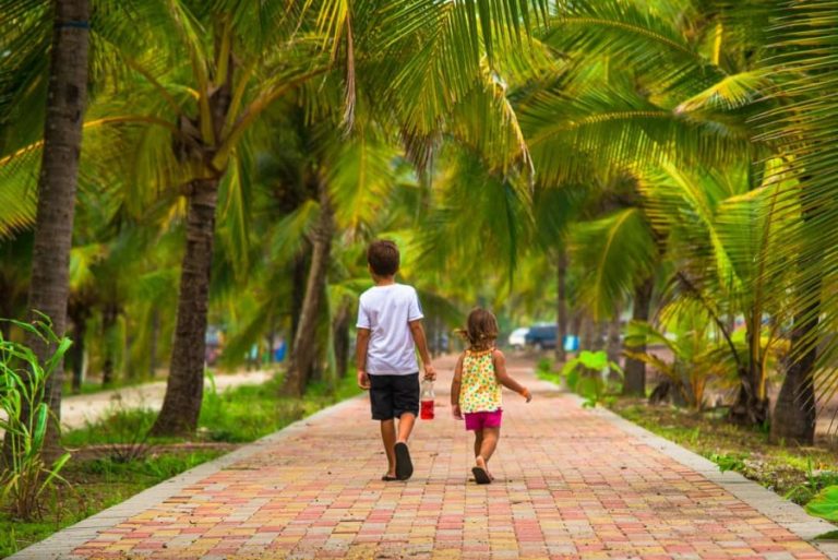 Twee kinderen lopen hand in hand over een tegelpad tussen hoge palmbomen in Costa Rica