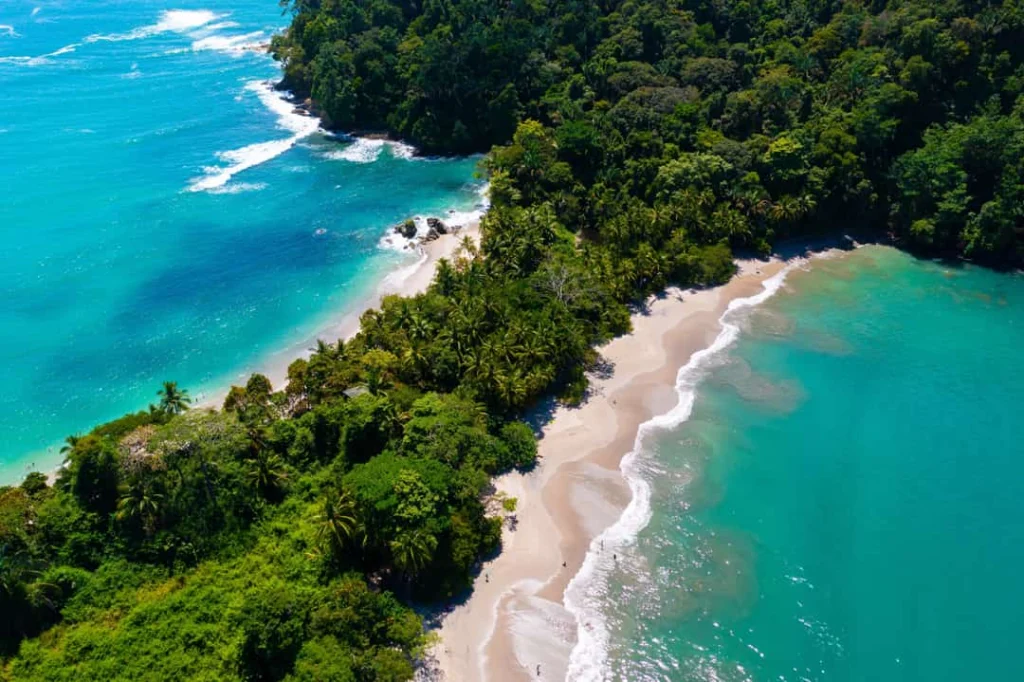 Luchtfoto van een groene landtong met jungle die uitloopt in een zandstrand tussen helderblauw en turquoise zeewater