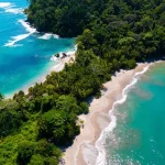 Luchtfoto van een groene landtong met jungle die uitloopt in een zandstrand tussen helderblauw en turquoise zeewater