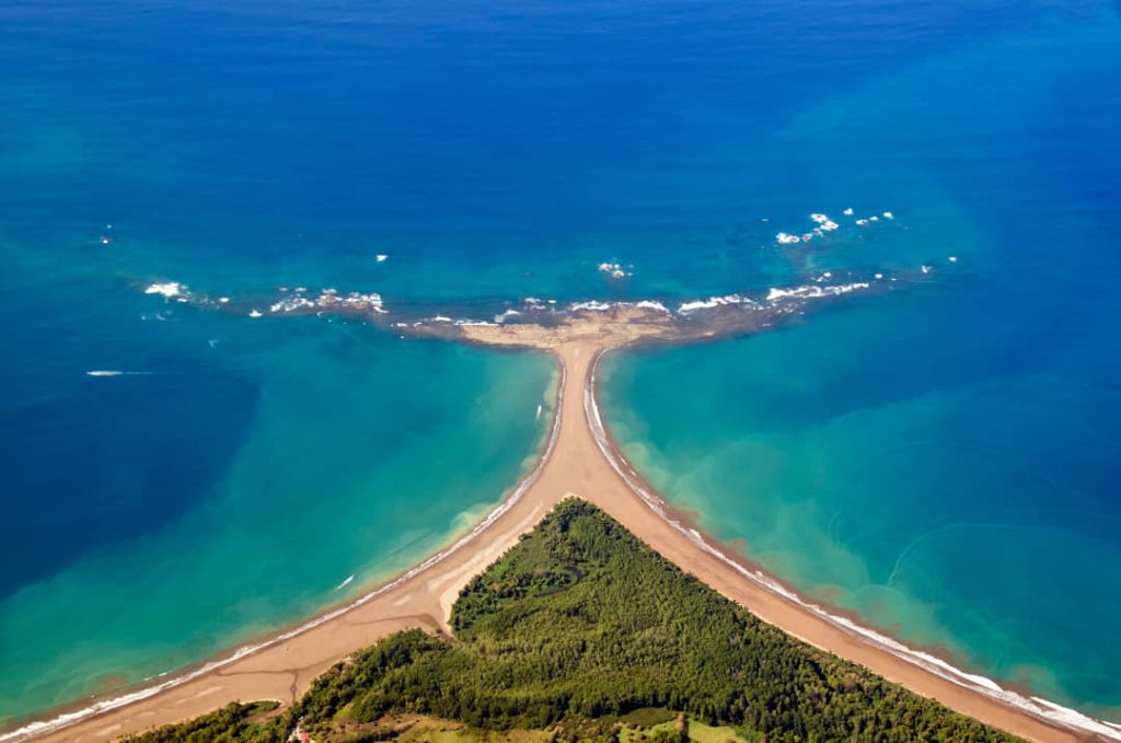 Luchtfoto van een groene landtong in Costa Rica die als een pijl tussen helderblauw en turquoise oceaanwater uitsteekt