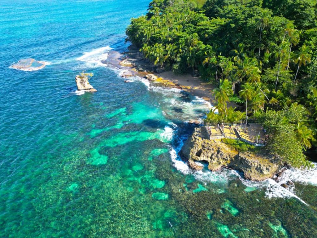 Luchtfoto van een met palmbomen begroeide rotsachtige landtong omringd door helder turquoise water