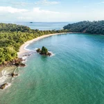 Luchtfoto van een baai met turquoise water, wit zandstrand en weelderig groen regenwoud bij Manuel Antonio National Park in Costa Rica