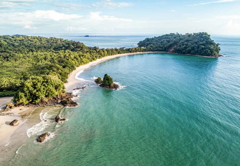Luchtfoto van een baai met turquoise water, wit zandstrand en weelderig groen regenwoud bij Manuel Antonio National Park in Costa Rica