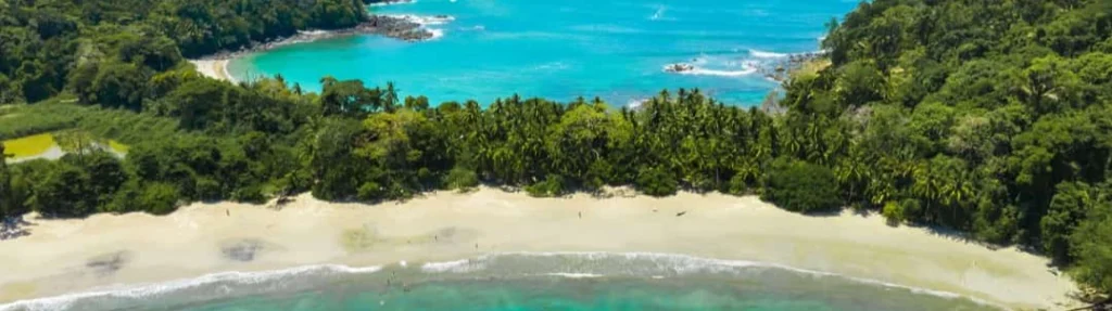 Luchtfoto van een wit zandstrand omzoomd door groene jungle, met een turkooizen baai en golven op de achtergrond in Costa Rica