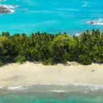 Luchtfoto van een wit zandstrand omzoomd door groene jungle, met een turkooizen baai en golven op de achtergrond in Costa Rica