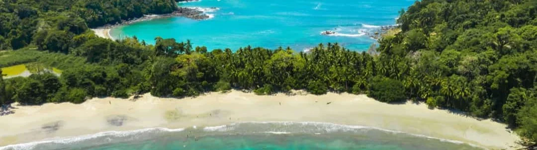 Luchtfoto van een wit zandstrand omzoomd door groene jungle, met een turkooizen baai en golven op de achtergrond in Costa Rica