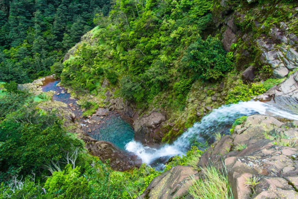 Luchtfoto van een waterval die uitmondt in kleine turquoise poelen tussen dicht bebost rotsachtig terrein