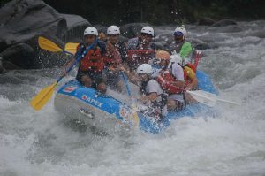 Een groep raften in een blauwe boot door kolkend wit water terwijl een hoge waterval vlakbij naar beneden stort