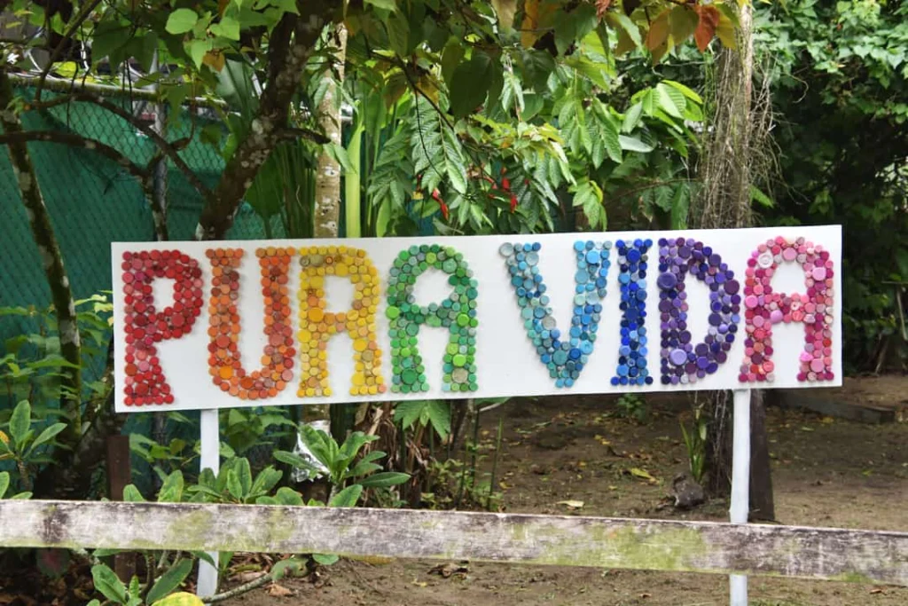 Kleurrijk bord met de tekst Pura Vida, samengesteld uit honderden gekleurde kroonkurken, tussen groene planten in Costa Rica