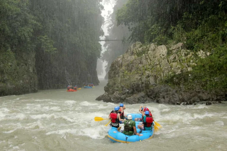 Een groep avontuurlijke raften in een blauwe rubberboot door wild stromend water tussen begroeide rotswanden in Costa Rica terwijl het regent