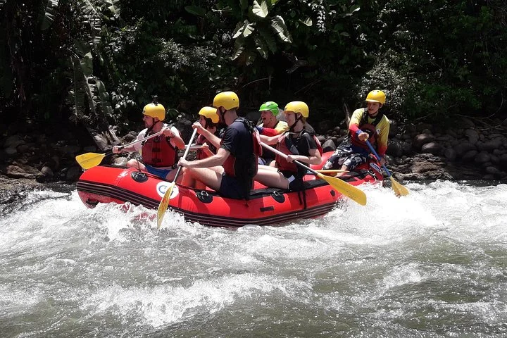 Een groep mensen met gele helmen en zwemvesten peddelt in een rode rubberboot door kolkend water op de Sarapiquí-rivier in Costa Rica