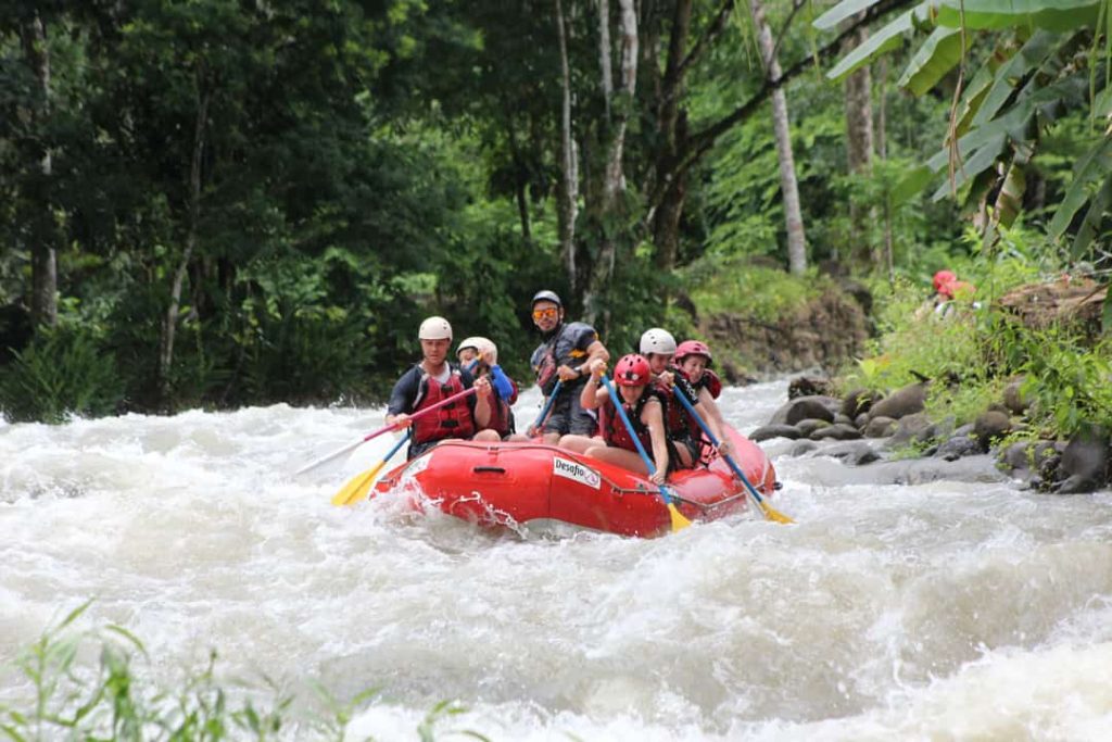Groep raftende reizigers vaart met een rode rubberboot over de Balsa-rivier tussen dicht bos in Costa Rica
