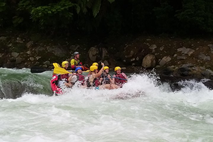 Groep raftende reizigers met gele helmen en peddels vaart met een rode rubberboot door schuimende golven op een rivier in Costa Rica