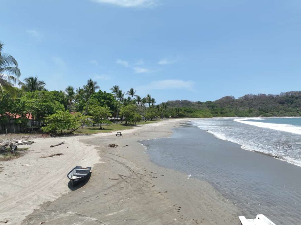 Vlak strand bij laag water met een aangemeerd bootje en huizen tussen palmbomen op de achtergrond in Costa Rica