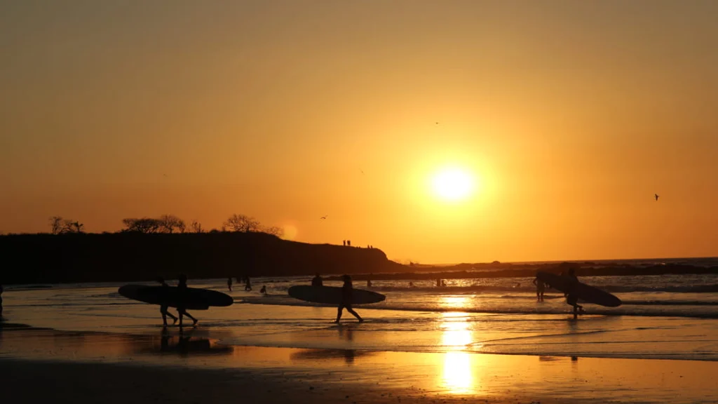 Silhouetten van surfers met surfplanken lopen over het strand van Tamarindo in Guanacaste tijdens een gouden zonsondergang