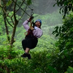 Een vrouw glijdt lachend aan een zipline door het groene regenwoud van Costa Rica