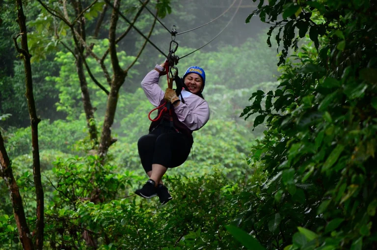 Een vrouw glijdt lachend aan een zipline door het groene regenwoud van Costa Rica