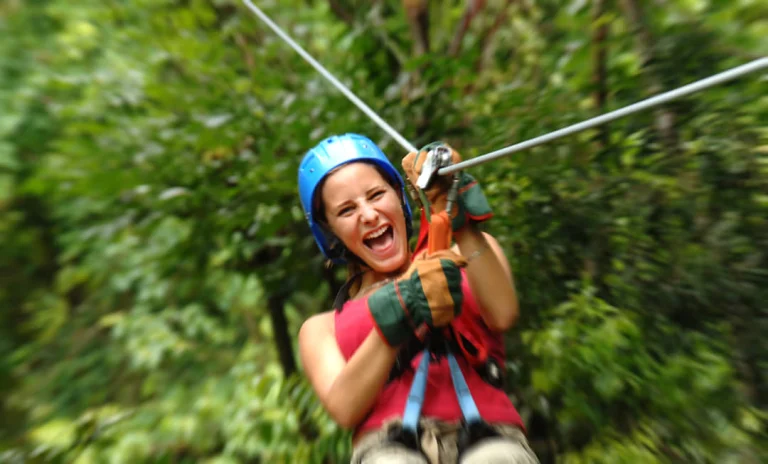 Een lachende vrouw met blauwe helm en handschoenen glijdt door een zipline tussen groen regenwoud in Costa Rica