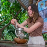Lachende vrouw draait aan een handmolen om cacaobonen te malen tijdens een chocoladetour in de jungle