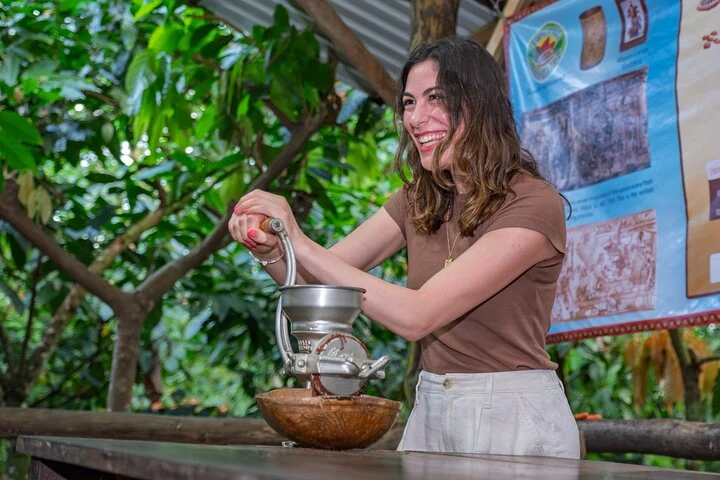 Lachende vrouw draait aan een handmolen om cacaobonen te malen tijdens een chocoladetour in de jungle