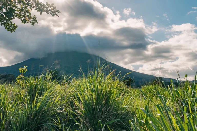 Een vulkaan in Costa Rica verscholen achter dikke wolken met zonnestralen, omgeven door hoog groen gras