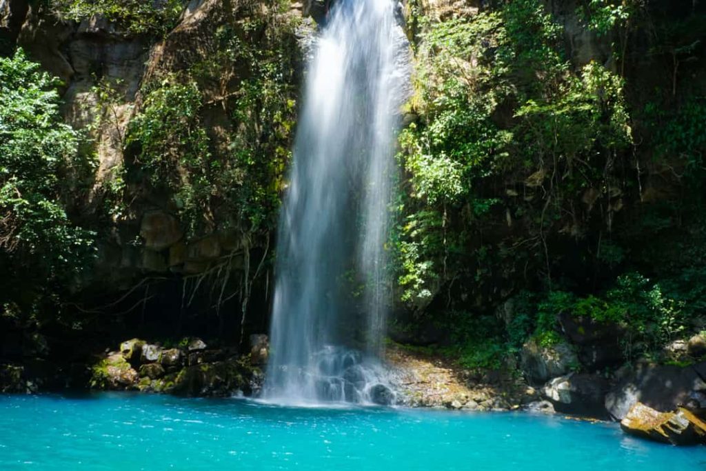Smalle waterval stort zich tussen rotsen in een helderblauwe poel omringd door dicht groen regenwoud