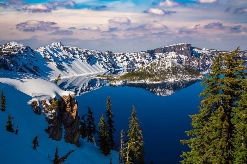 Diepblauw meer van Crater Lake omringd door besneeuwde kraterwanden en dennenbomen op een heldere winterdag in Oregon