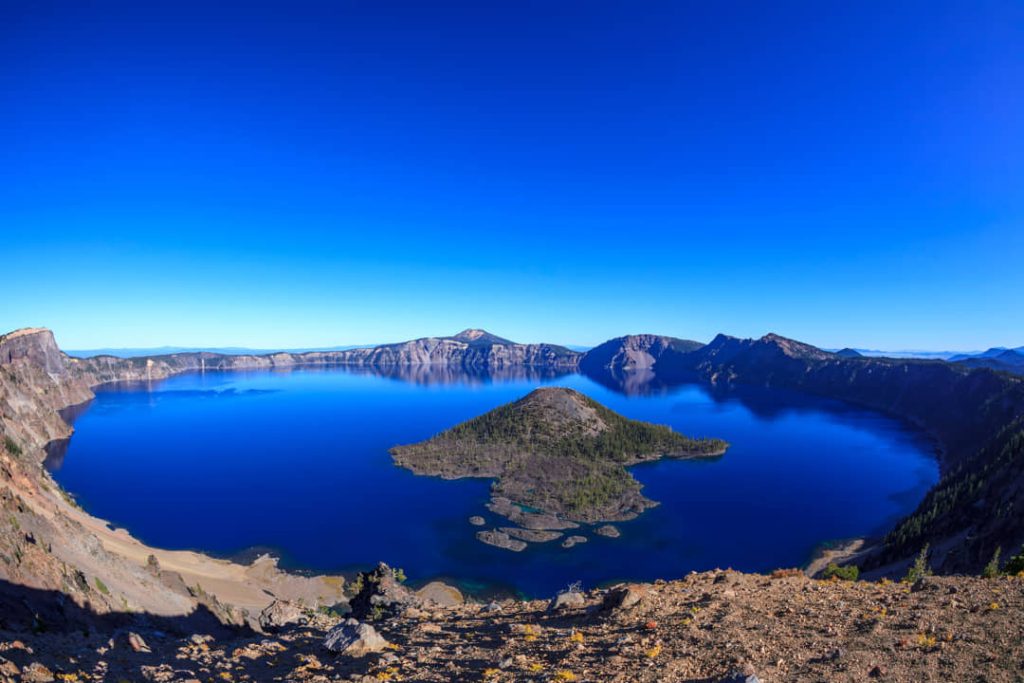 Breed panorama van het diepblauwe water van Crater Lake met Wizard Island in het midden en kraterwanden aan alle kanten in Oregon