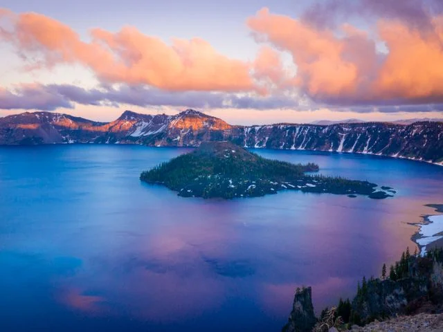 Vulkanisch eiland Wizard Island in het intens blauwe water van Crater Lake met roze wolken bij zonsondergang in Oregon