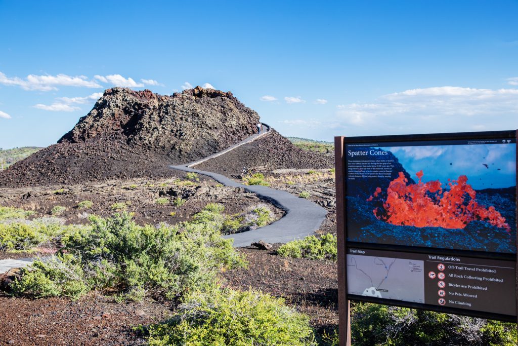 Een spatter cone van gestold lava met een geasfalteerd pad ernaartoe en een informatiebord over de vorming ervan op de voorgrond