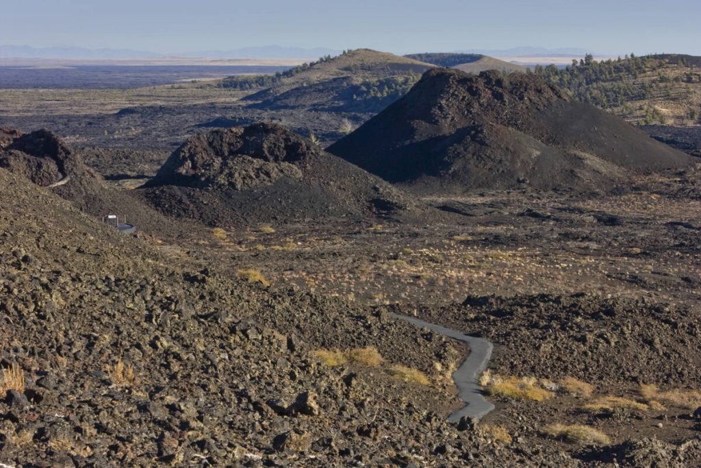 Smalle asfaltweg slingert tussen zwarte vulkanische kegels en een uitgestrekt lavaveld in Craters of the Moon National Monument