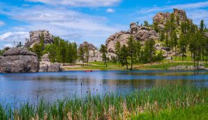 Helderblauw meer omringd door hoge granieten rotsformaties en dennenbos, met een kanovaarder op het water in South Dakota