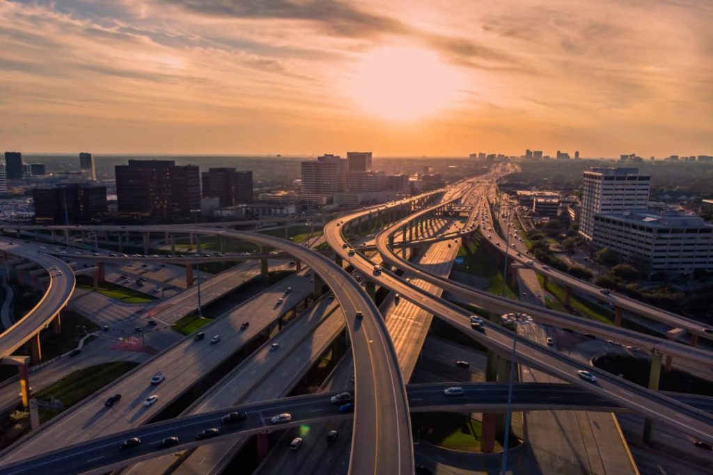 Luchtfoto van gebogen snelwegen die door elkaar heen lopen bij zonsondergang, met de skyline van Dallas op de achtergrond