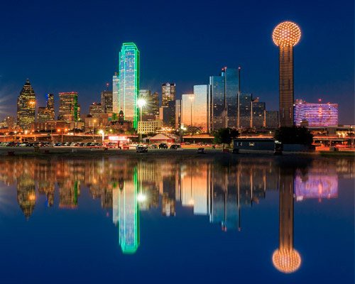 Verlichte wolkenkrabbers van Dallas waaronder de bolvormige Reunion Tower, weerspiegeld in kalm water bij nacht