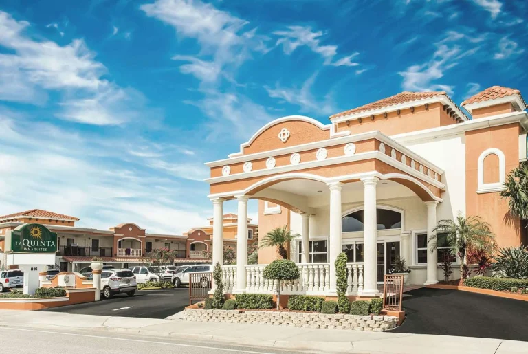 Ingang met witte zuilen en oranje gevel van hotel La Quinta Inn & Suites in Daytona Beach onder een blauwe lucht