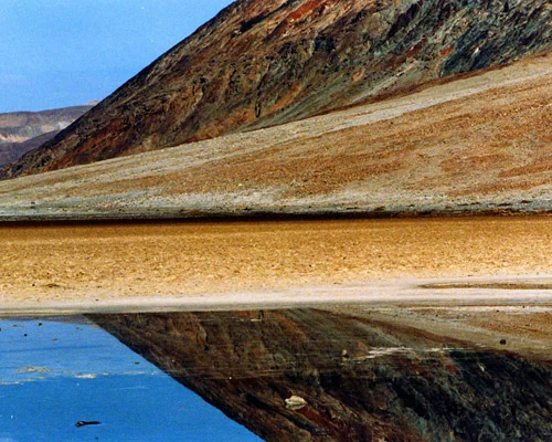 Zoutvlakte van Badwater Basin die overgaat in een dun laagje water dat de omringende bergen weerspiegelt in Death Valley National Park