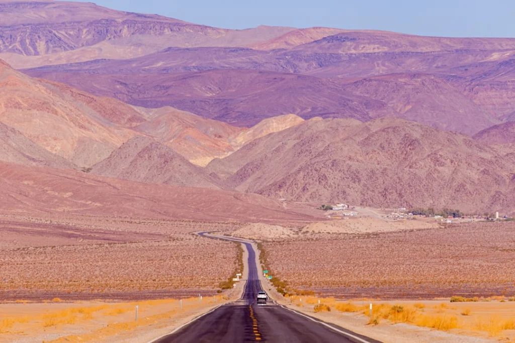 Lege asfaltweg loopt kaarsrecht door een vallei met paarsgetinte gestreepte bergen op de achtergrond in Death Valley