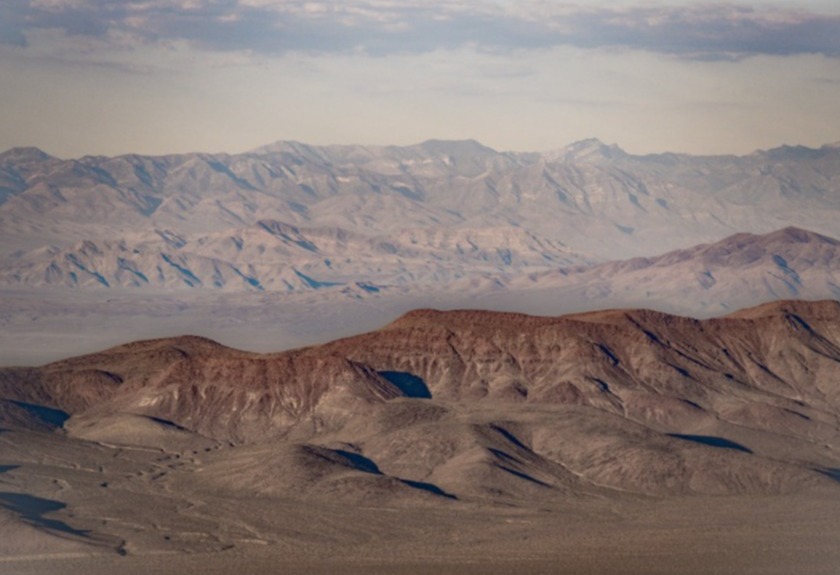 Gelaagde bruine en rode bergketens strekken zich uit tot aan de horizon in een wazige woestijnlucht bij Death Valley