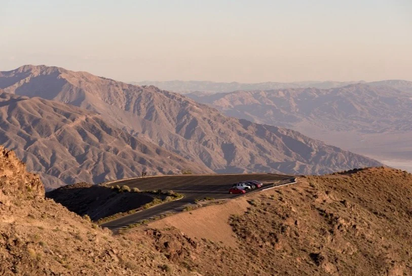Bochtige bergweg met een uitzichtpunt waar auto's geparkeerd staan boven een uitgestrekte woestijnvallei in Death Valley