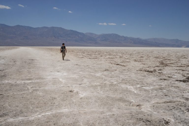 Eenzame wandelaar loopt over de witte gebarsten zoutkorst van Badwater Basin met bergen op de achtergrond in Death Valley