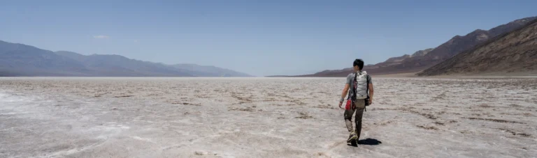 Een wandelaar met rugzak loopt over de witte zoutvlakte van Badwater Basin in Death Valley National Park, omringd door bergen