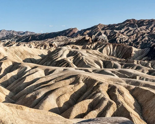 Golvend landschap van geelbruine, sterk geërodeerde heuvels met bergen op de achtergrond bij Zabriskie Point in Death Valley National Park