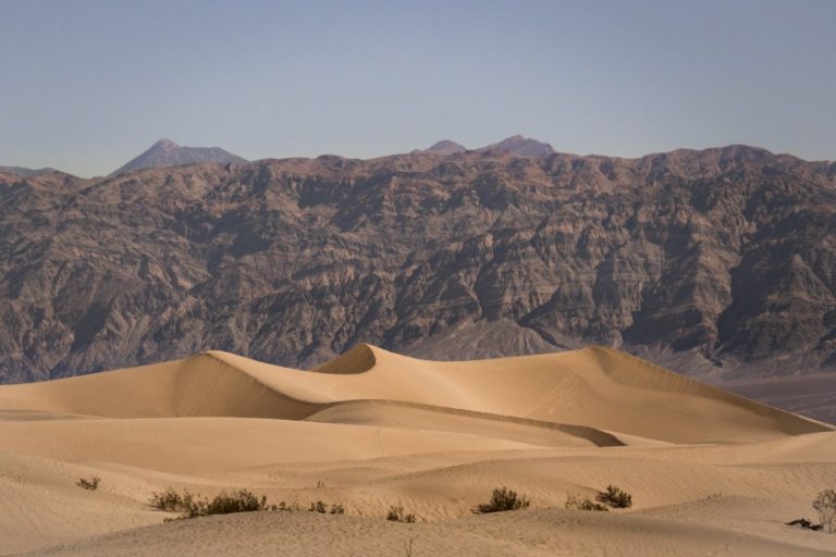 Kale zandduinen met zachte schaduwen liggen voor een ruige gestreepte bergketen in Death Valley
