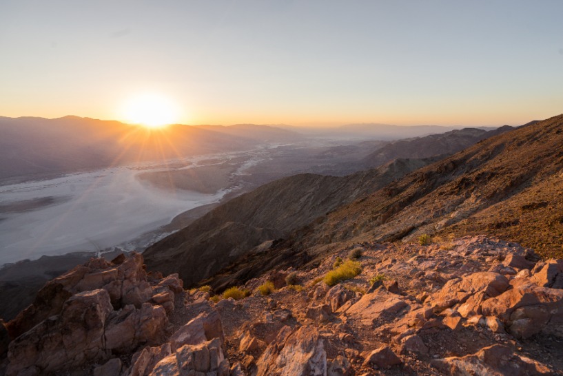 Opkomende zon werpt een warm licht over een rotsachtige berghelling met uitzicht op een zoutvlakte in de vallei van Death Valley