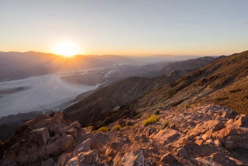 Opkomende zon verlicht een uitgestrekte zoutvlakte gezien vanaf een rotsachtig uitkijkpunt hoog boven Death Valley