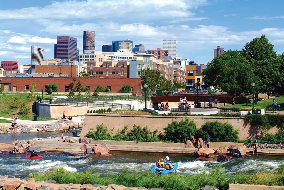 Mensen kajakken en raften op de rivier in Confluence Park in Denver, met de skyline van de stad op de achtergrond