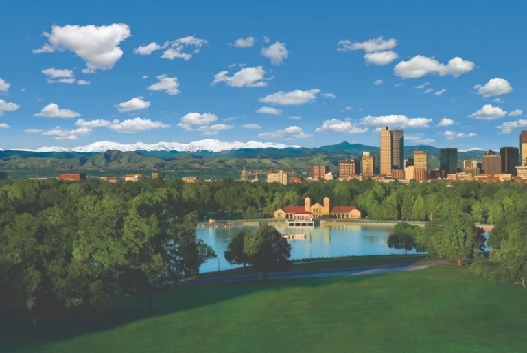 Uitzicht over een groen park met vijver in Denver, met de skyline van de stad en besneeuwde Rocky Mountains op de achtergrond