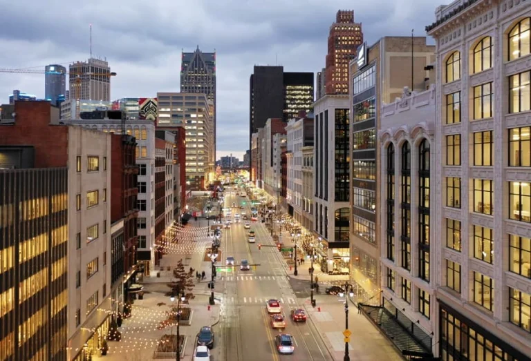 Uitzicht op een drukke straat in Detroit met verlichte wolkenkrabbers en rijdende auto's tijdens de schemering